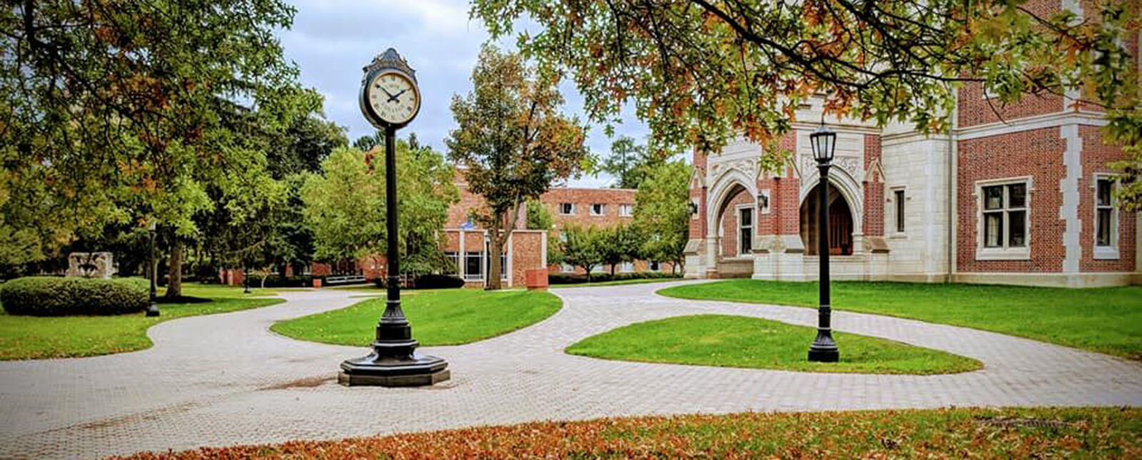 一座钟矗立在迈尔大厅附近的校园走道中央，地上铺着彩色的树叶