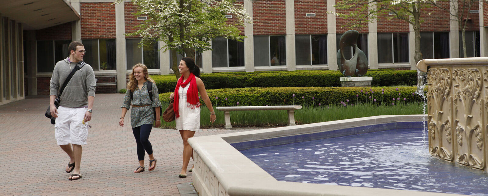 两名女学生和一名男学生在喷泉边走边聊天