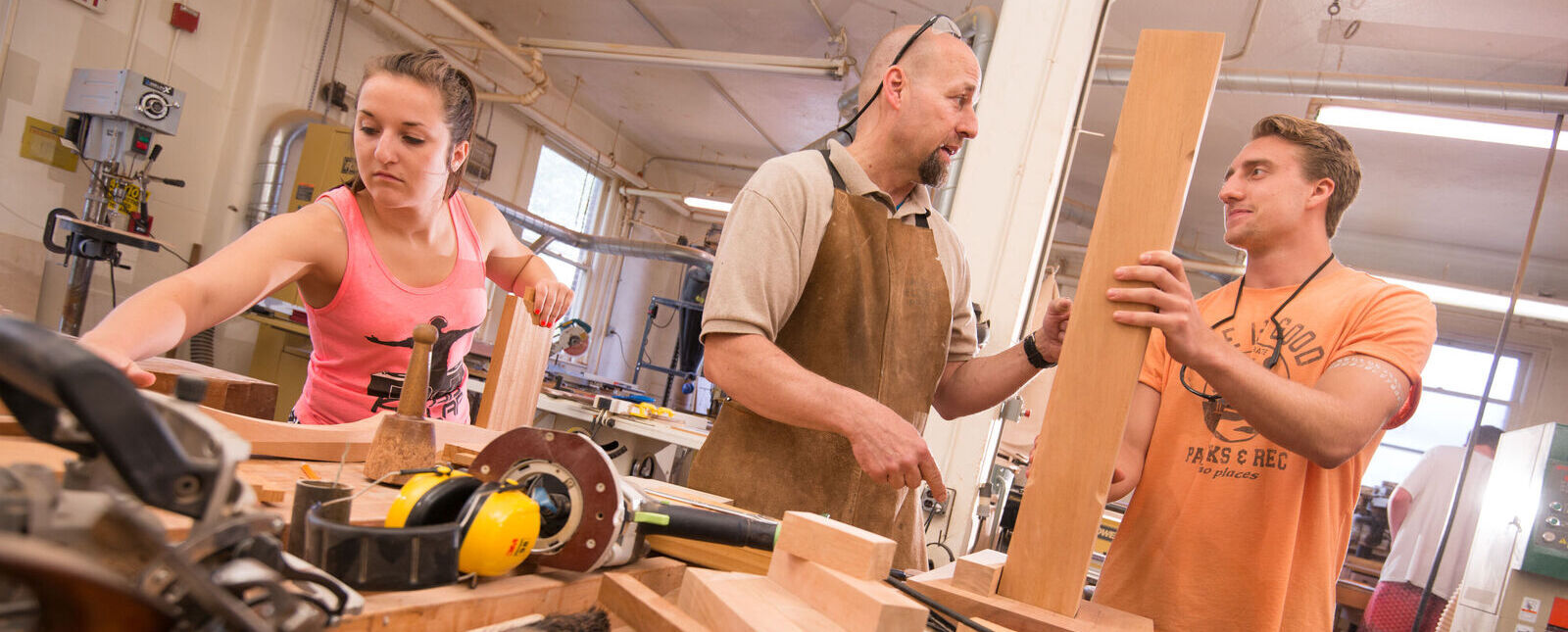 An art faculty member works with students on wood projects