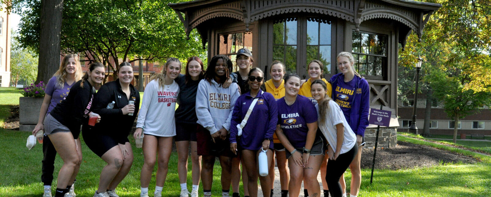The Mark Twain Study is pictured in front of a line of trees while students pose in front of the study. 