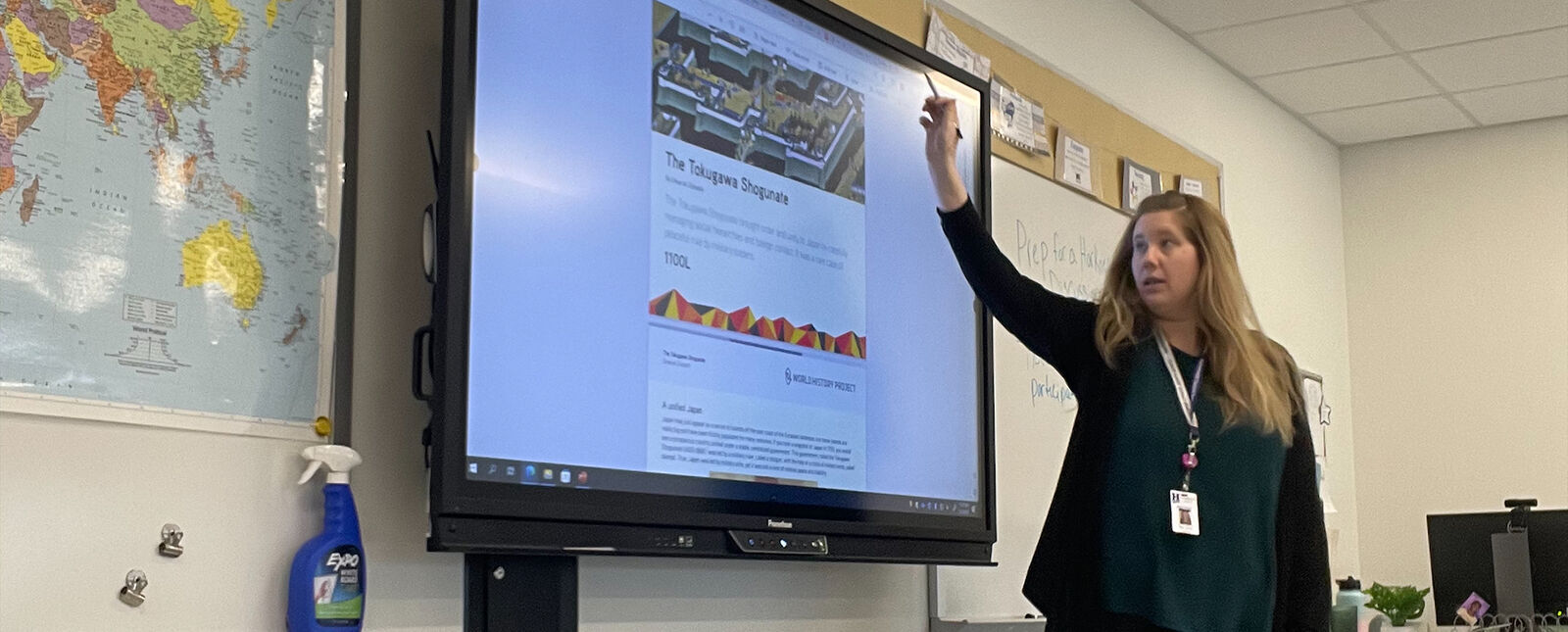 A female student teacher points to a smartboard in a classroom