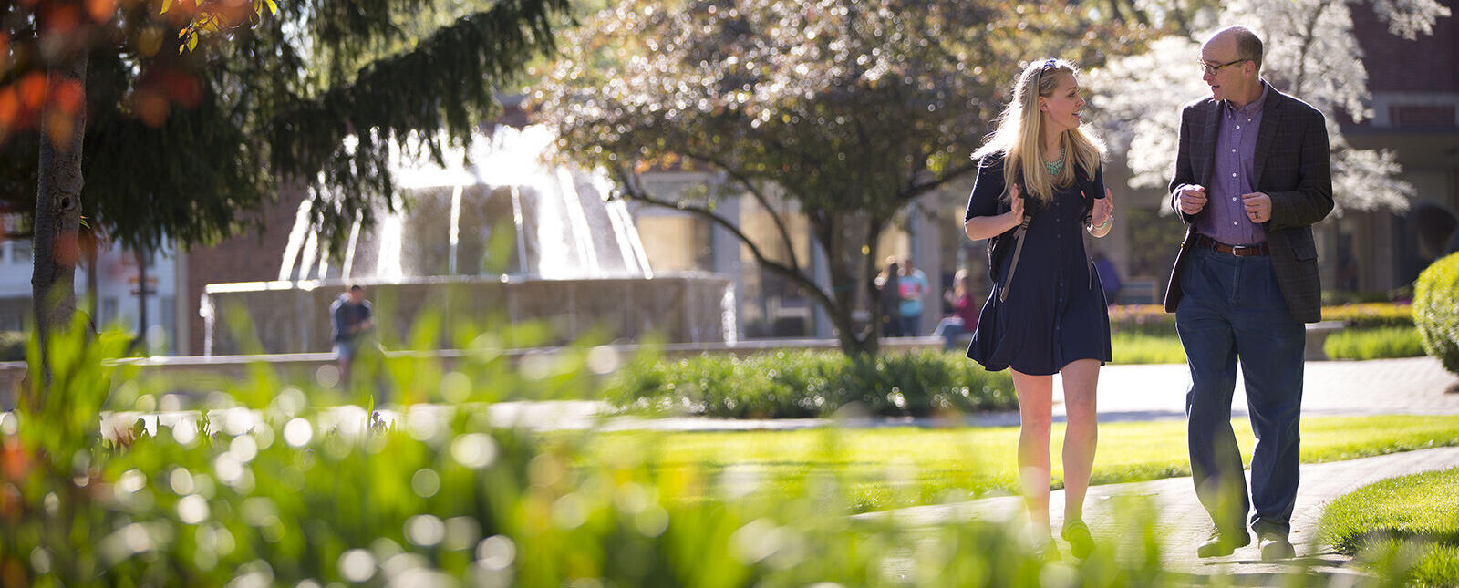 A female student speaks with a male professor while walking across the Elmira College campus