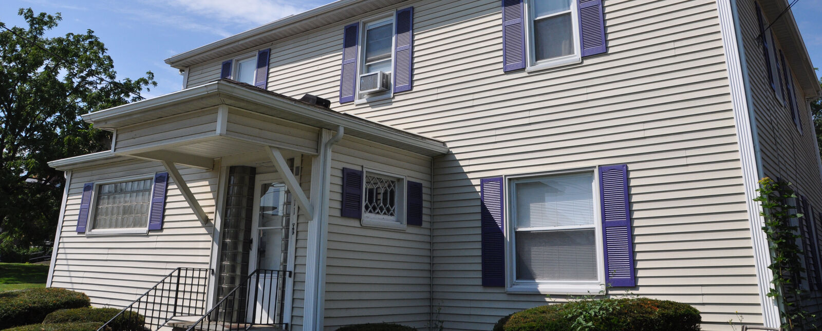 The exterior of the Alumni House with tan siding and purple shutters.
