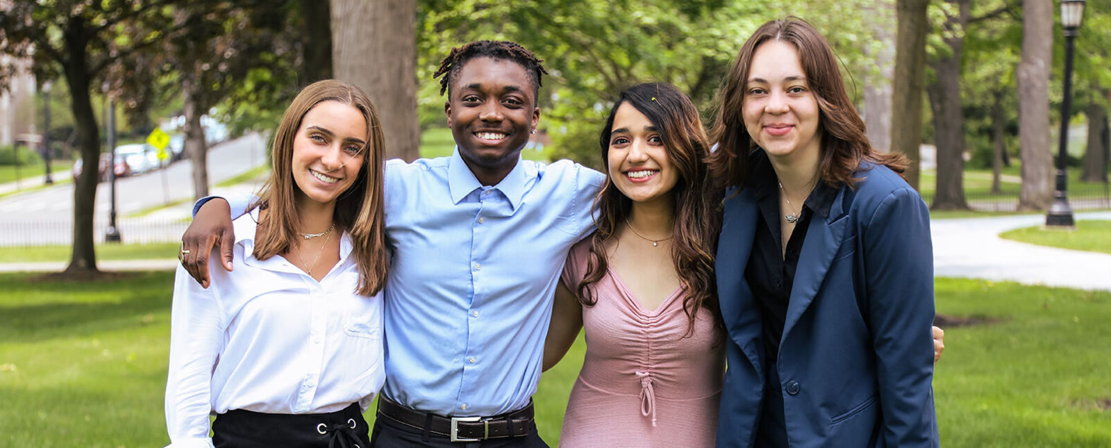 A male and three female business students pose for a picture together outside on the Elmira College campus