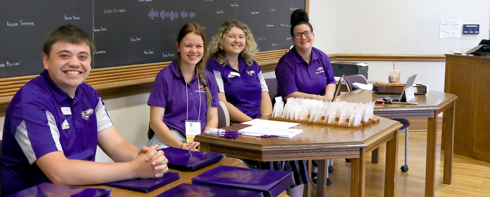 Admissions staff and helpers smile at greeting tables during Summer Orientation