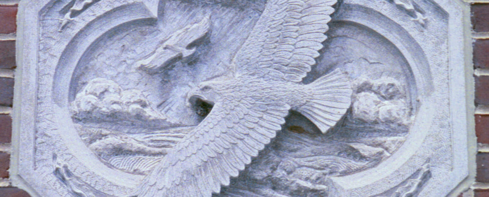 An octagon stone with an engraving of an eagle and scenery is mounted on a brick wall