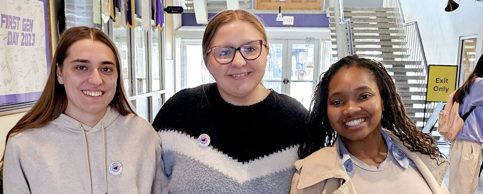 Three female students smile together in the Campus Center lobby 