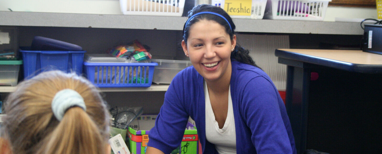 A female student teacher smiles while working in a classroom with a student