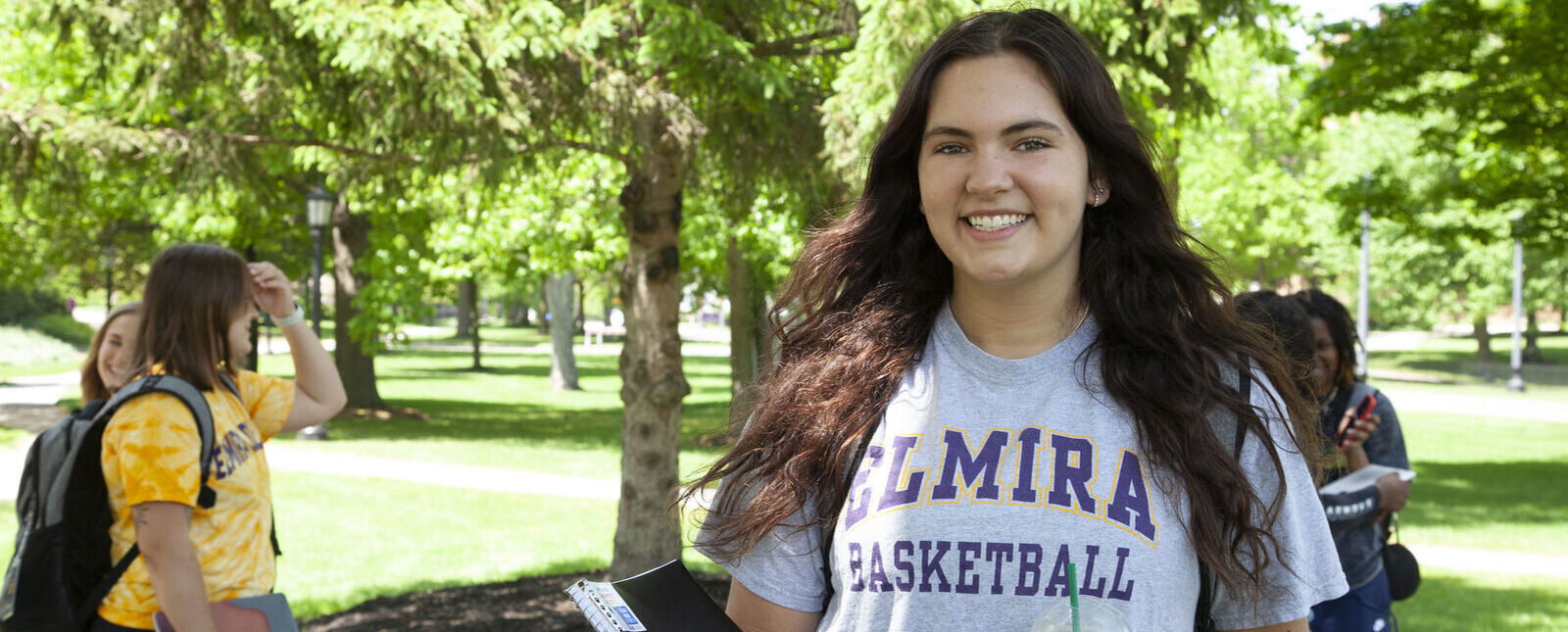 A female student smiles for a picture while walking outside on the Elmira College campus