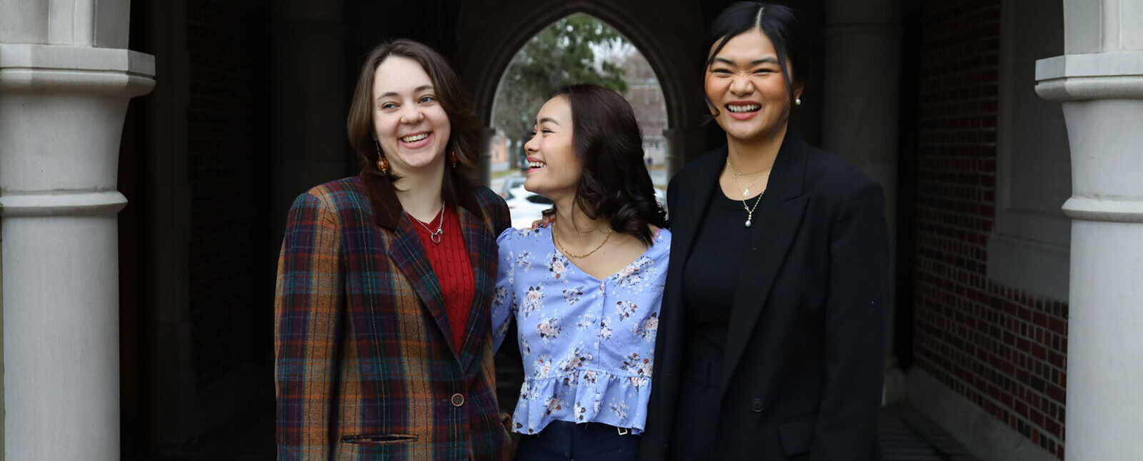 Three female students smile while under the archway at Meier Hall