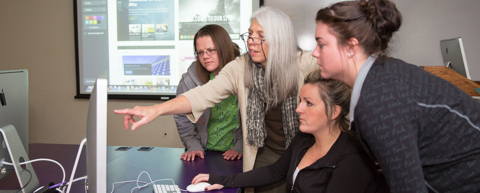 A faculty member helps three female students at a computer