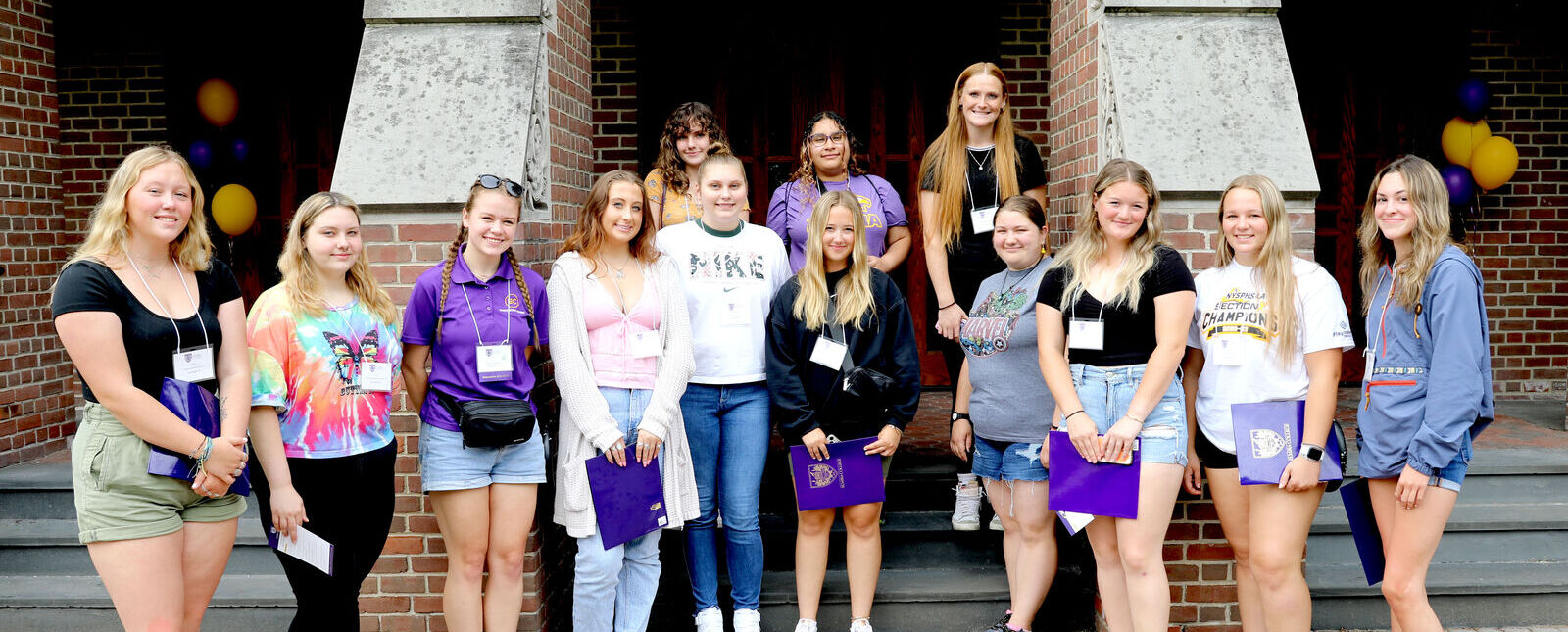 A group of students and an orientation leader pose on the steps leading up to the Gibson Theatre entrance during an orientation event