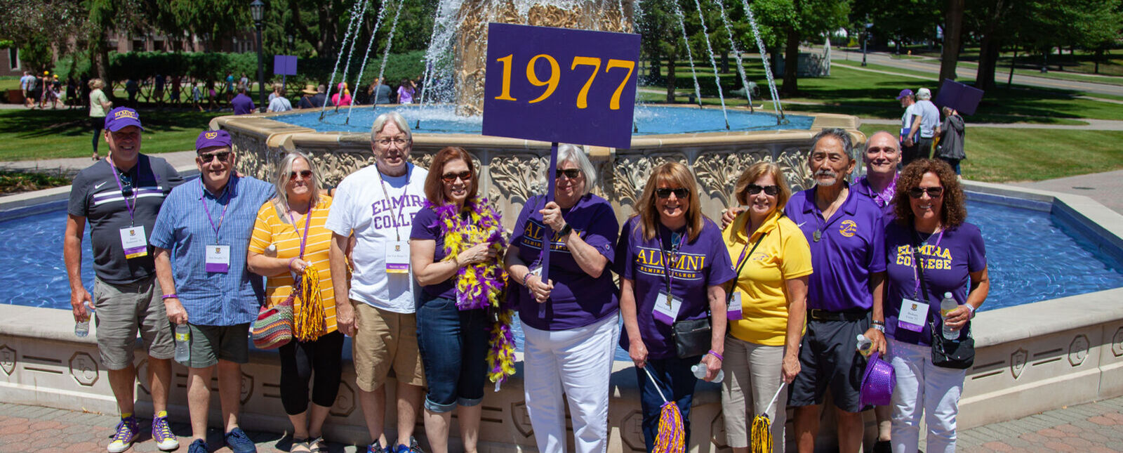 Members of the Class of 1977 stand in front of the fountain with a 1977 sign during reunion