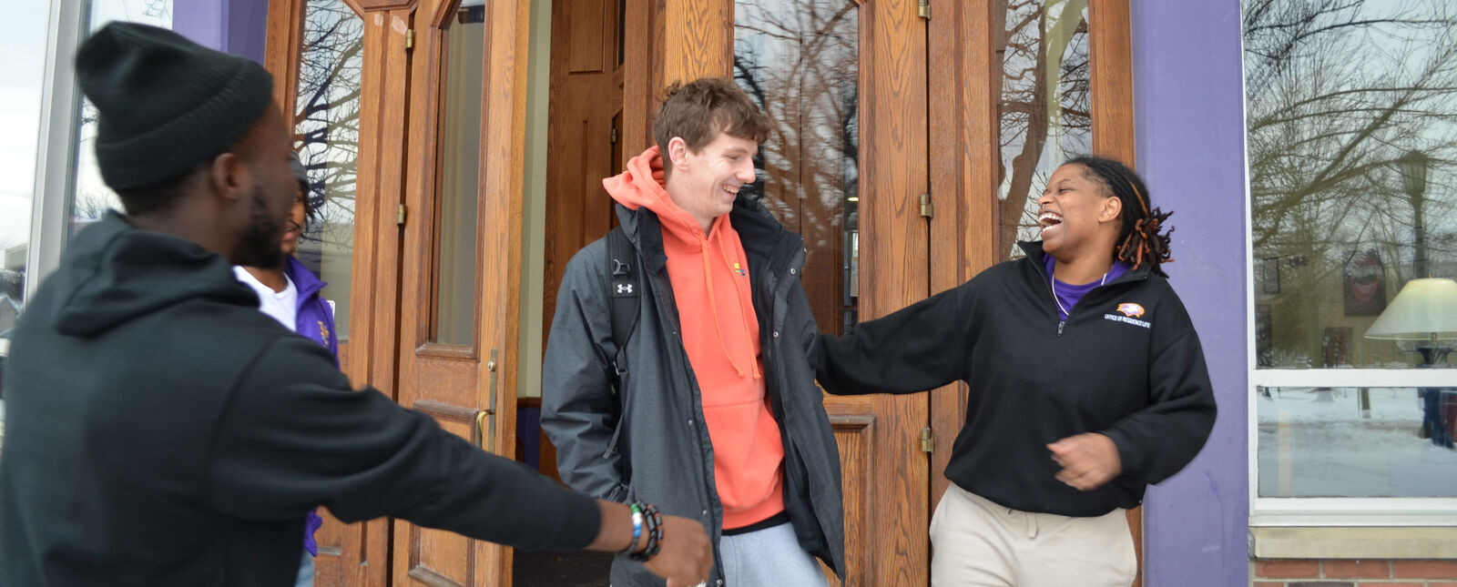 Students share smiles and laughs at the entrance to a residence hall