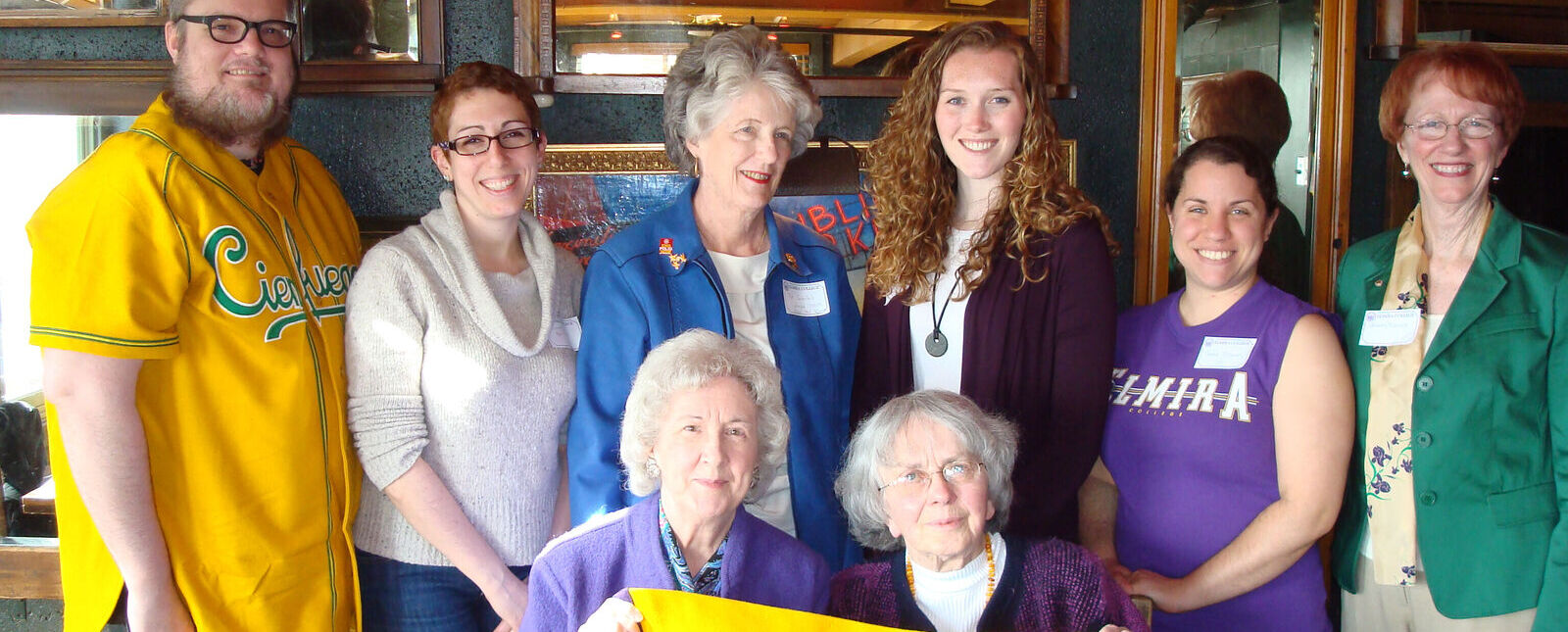 A group of Elmira College alumni from the Seattle area are pictured with a purple and gold EC banner during an alumni event