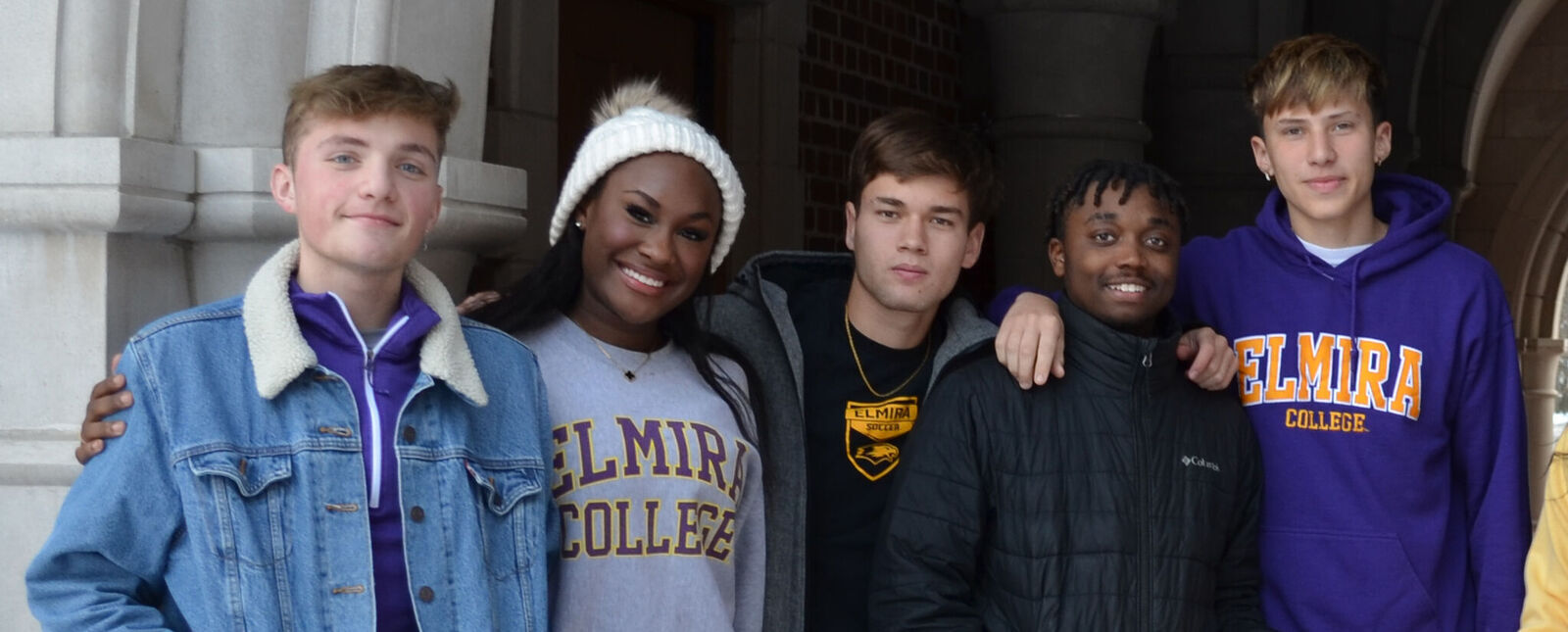 A group of students smile while standing in the archway of Meier Hall