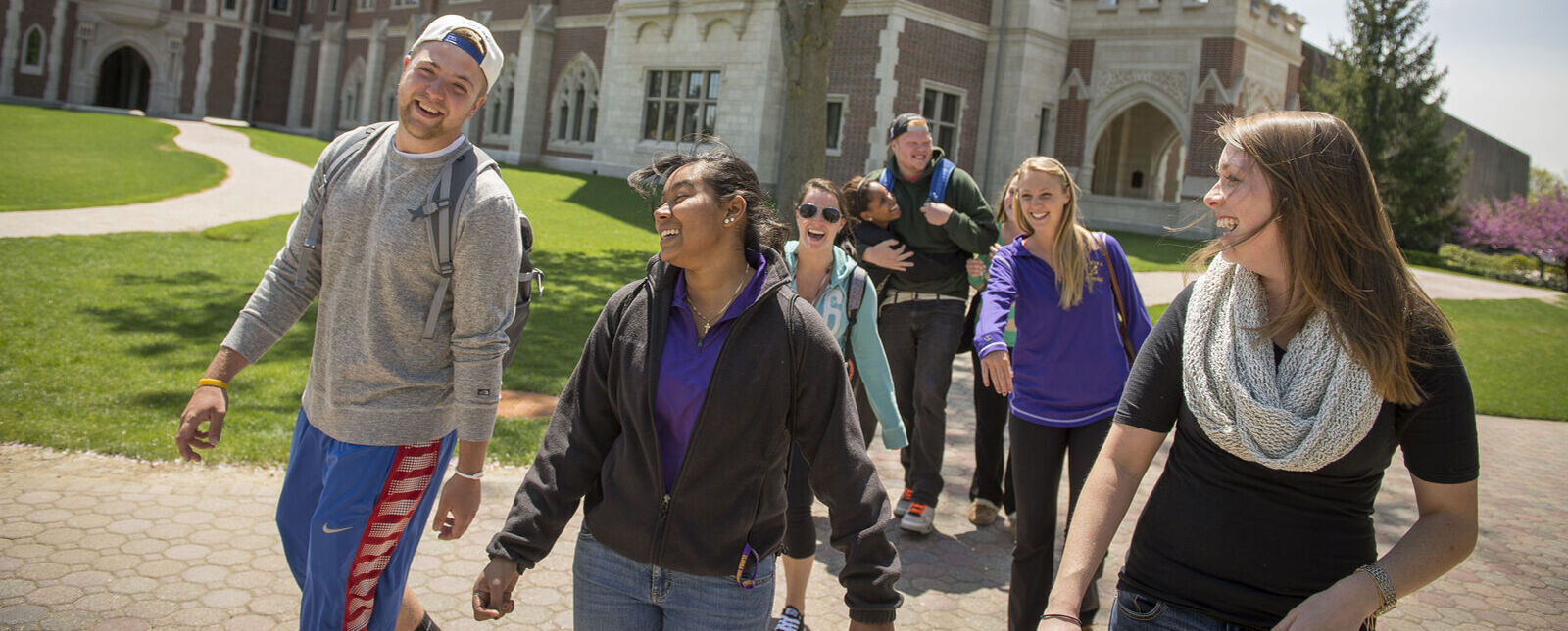 A group of students smile and laugh as they walk across the Elmira College campus