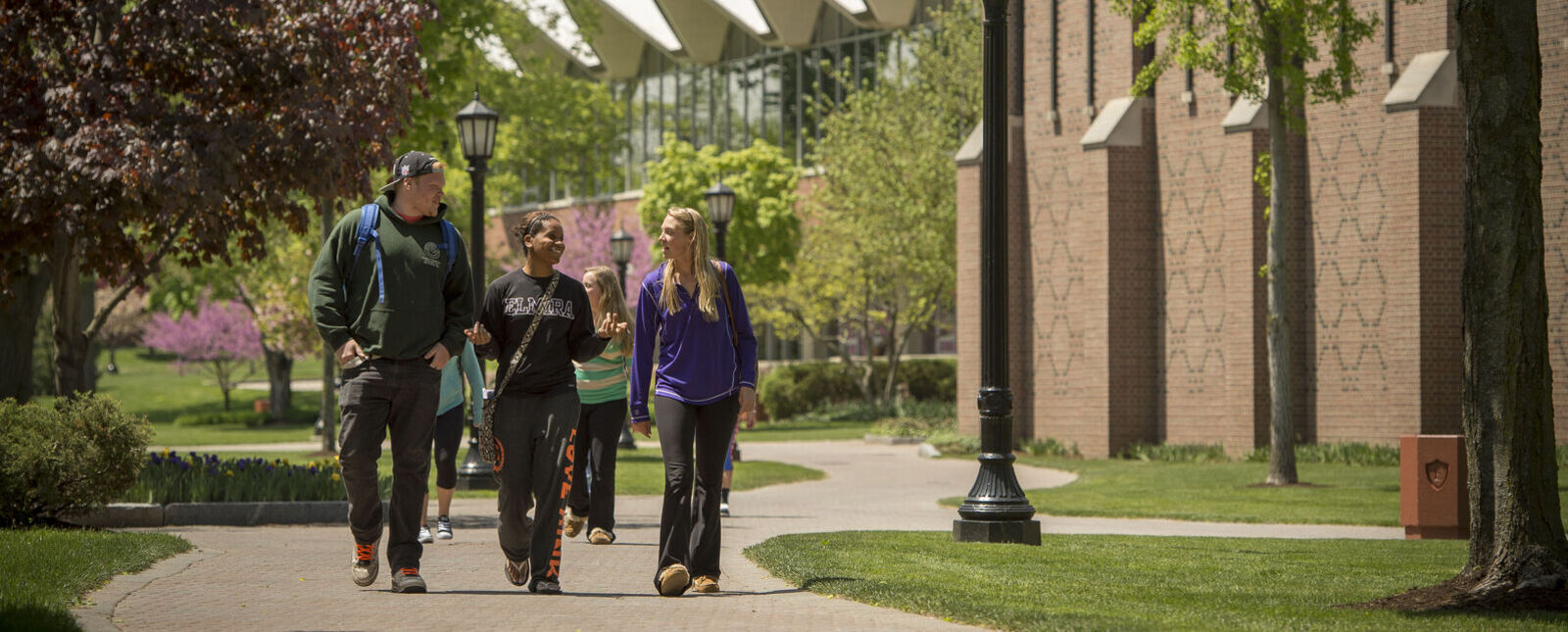 A male student and two female students talk while walking through the center of campus