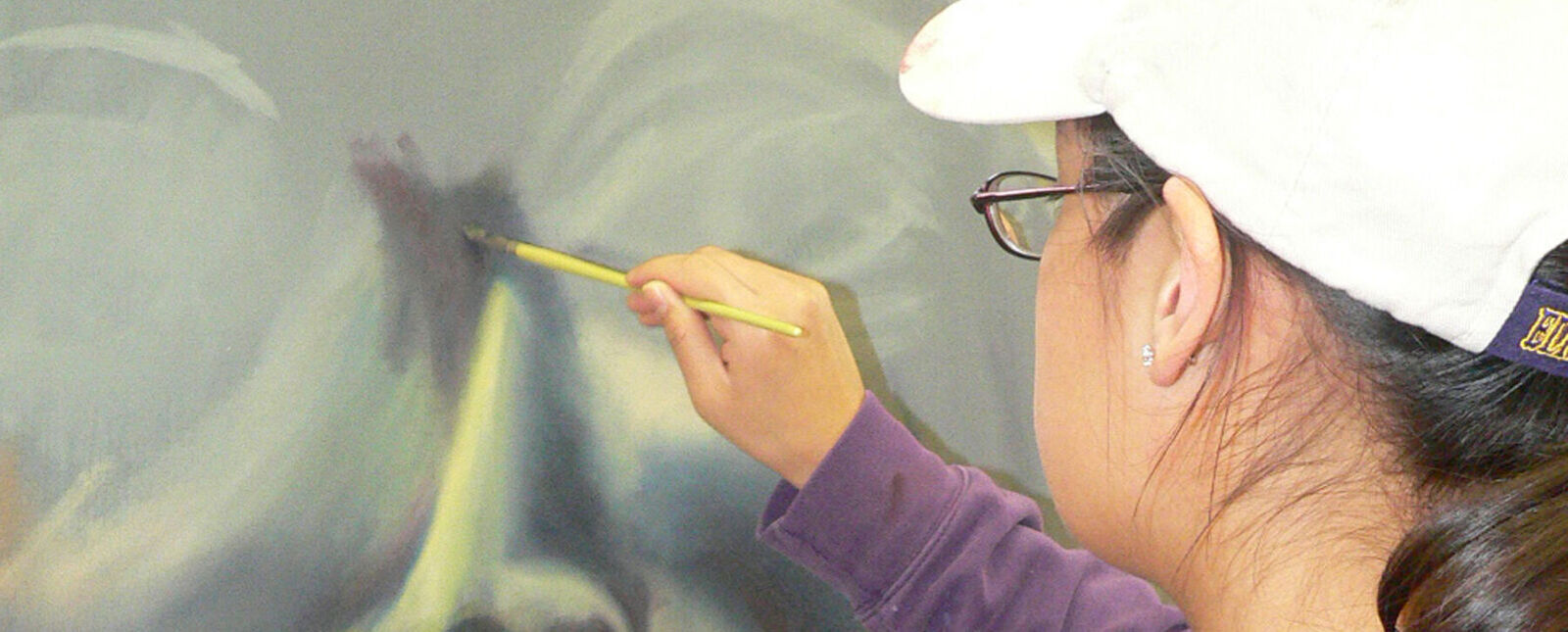 A female student paints a portrait on a large canvas