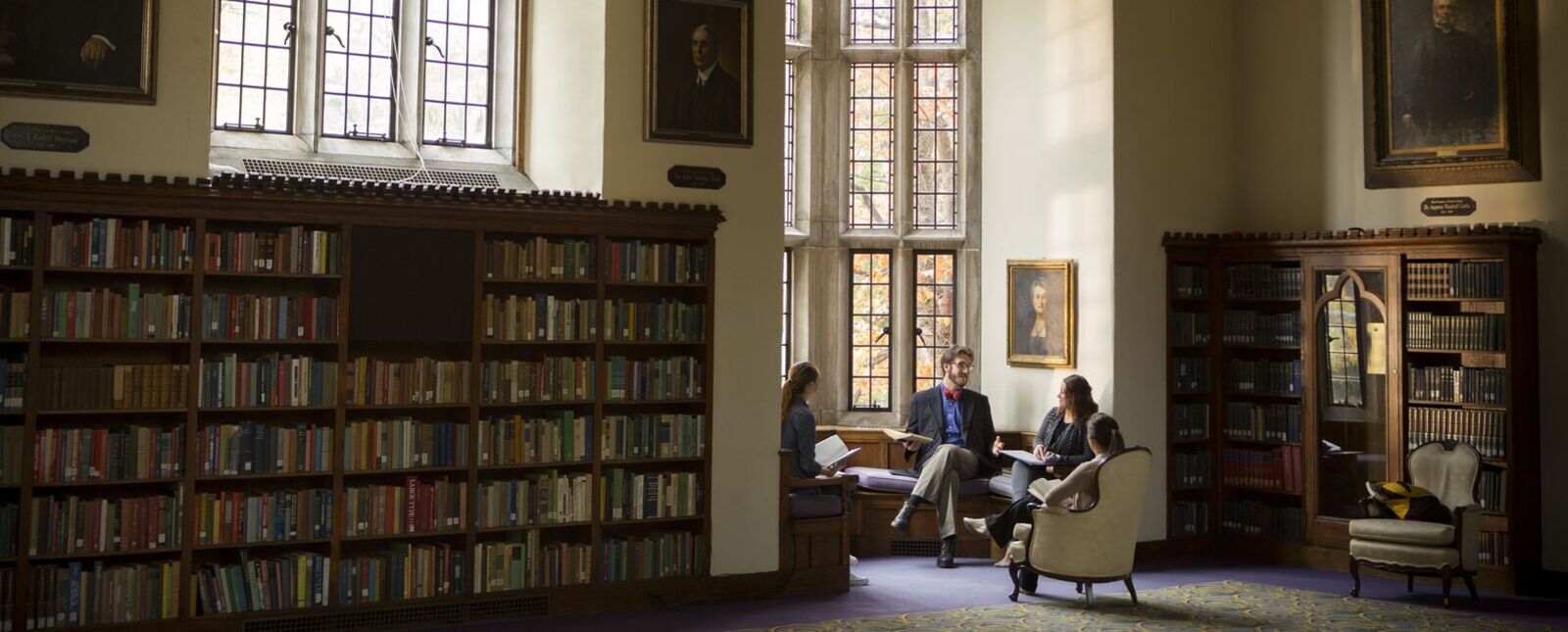 Students sit in and around a window bay between bookcases in Hamilton Hall