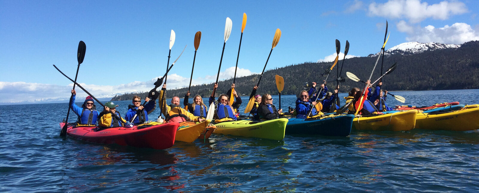 A group of students and faculty raise their paddles into the air as they kayak in Alaska