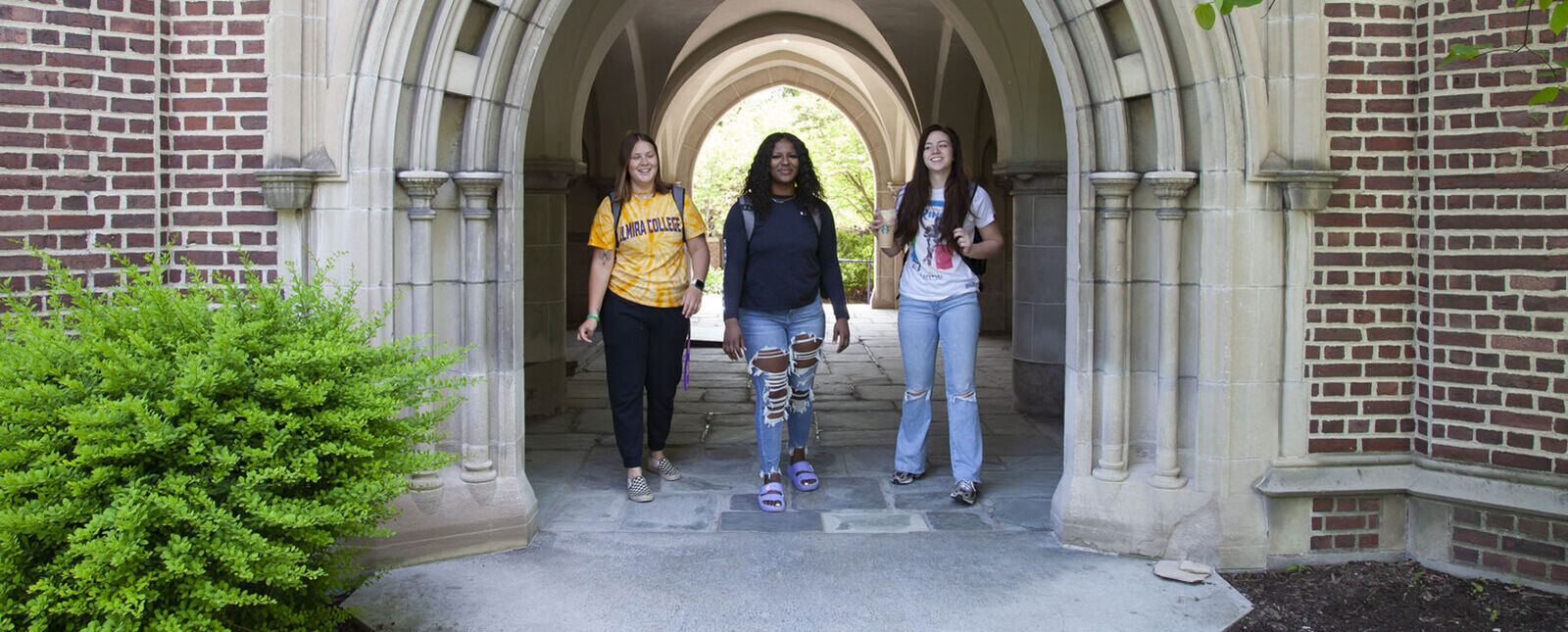 Three female students stand under the stone archway leading to the entrance of Meier Hall