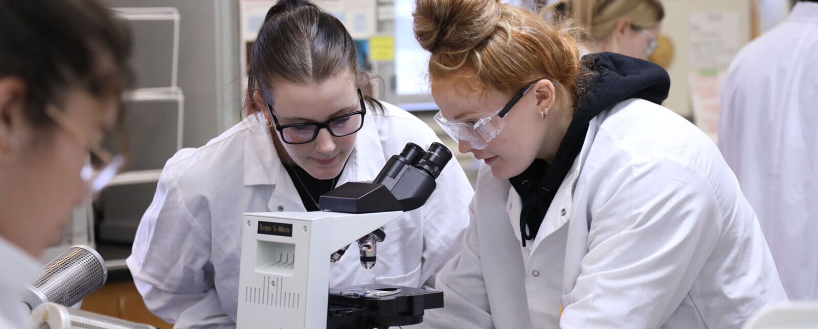 Two female students work around a microscope in a lab