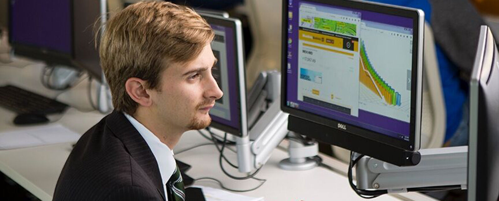 A student in a suit studies financial information on a computer in the Malesardi Financial Trading Room