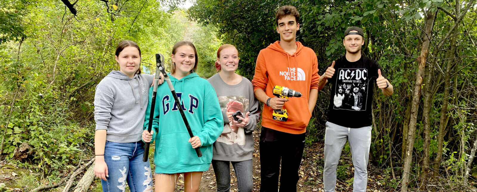 A group of Environmental Science students stand together while holding tools in a wooded area.